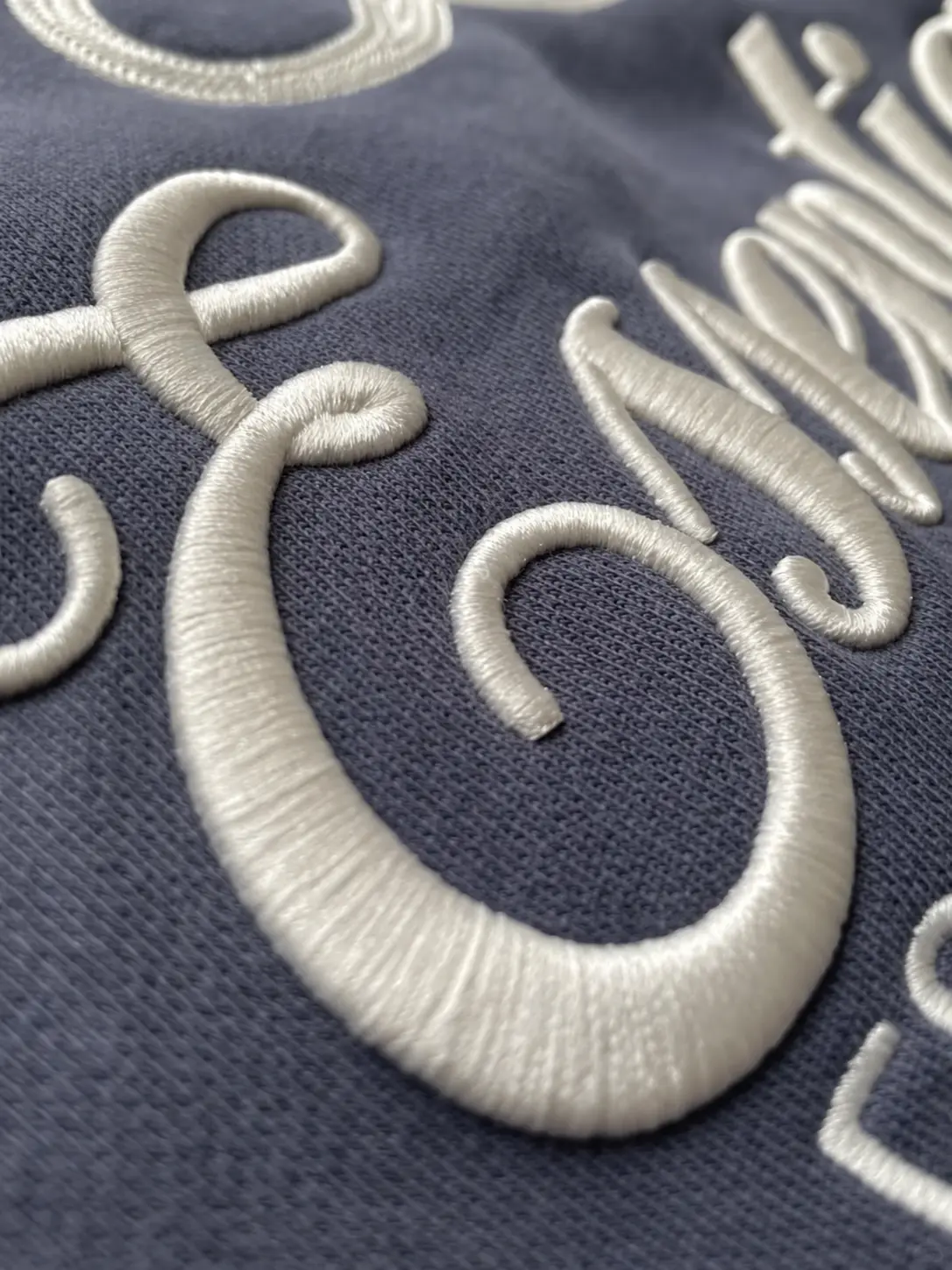 Cream raised stitched lettering with smooth thread coverage on grey-blue knit fabric
