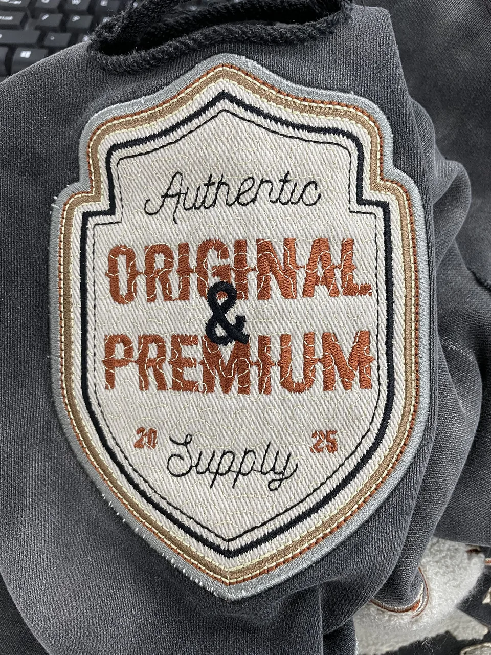 Cream, rust and black embroidered patch on a grey garment sample